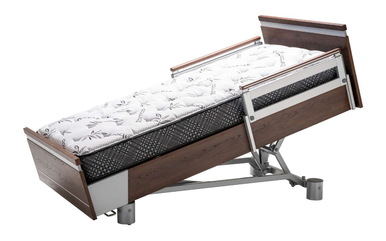 A hospital bed with an adjustable frame is tilted at an angle. It features wooden panels on the head and foot, with a patterned mattress on top.