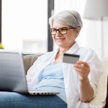 A woman utilizing a laptop while making an online purchase with her credit card from the comfort of an electric adjustable bed, highlighting its health advantages for seniors.