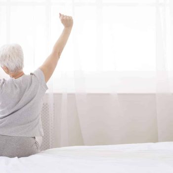 A woman raising her arms on a bed, contemplating hospital bed choices for home use.